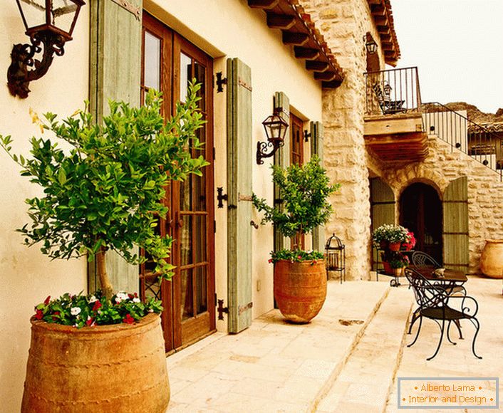 Патио в средиземноморском стиле украшают горшки с живыми растениями. Привлекательный дизайн, мебель с витиеватыми спинками, керамические горшки создают уютную, расслабляющую атмосферу. 