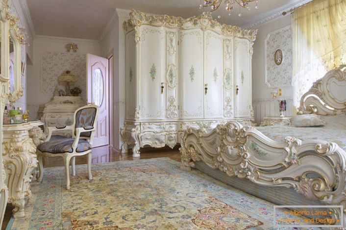 Снежно бела спаваћа соба са резбареним масивним намештајем од дрвета. Кревет са високом плафонском плочом на плочи, елегантно се уклапа у ентеријер у барокном стилу.
